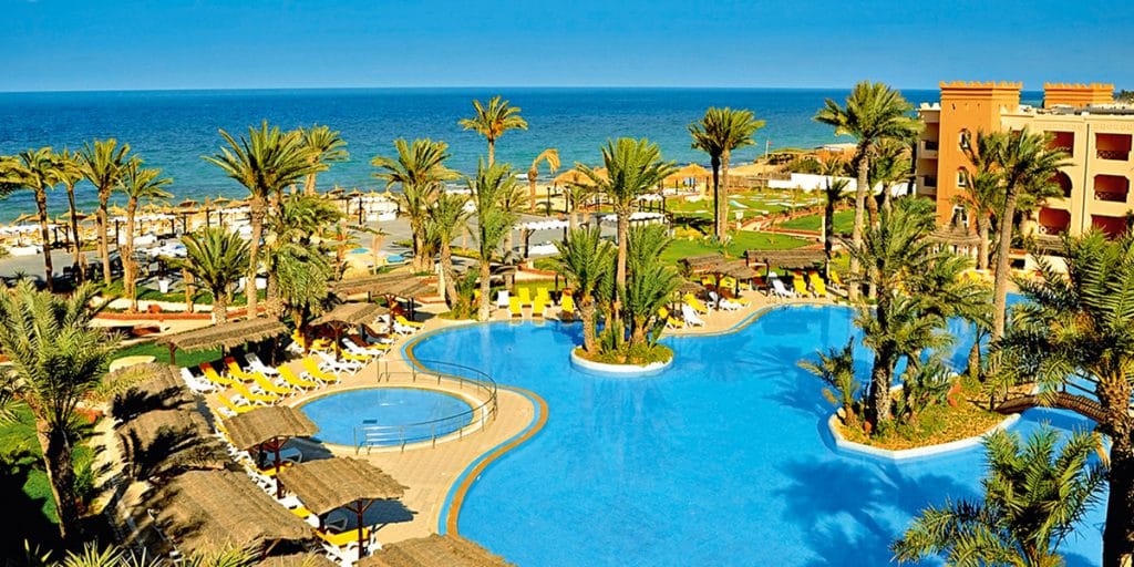 Vue aérienne de l'hotel Vincci Palms à Djerba : palmiers au milieu d'une grande piscine extérieure face à la mer.