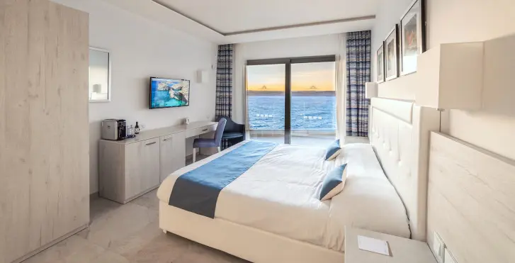Chambre hôtel Ramla bay resort à Malte. Lit double  avec vue sur la mer et écran plat fixé sur le mur.