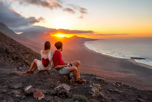 Jeune couple profitant du beau coucher de soleil assis sur la montagne avec vue magnifique sur le littoral de Cofete sur l'île de Fuerteventura aux îles Canaries.