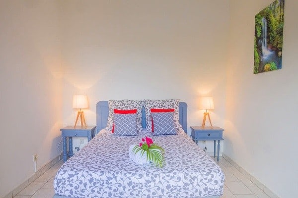 Chambre  avec lit double pour couple Alamanda Jaune en Guadeloupe. Lit avec décoration tropicale + fleur sur le lit  et tableau de chute d'eau sur le mur.