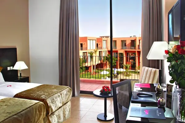 Chambre spacieuse avec deux lits et terrasse + vue de la piscine cernée de palmiers. 