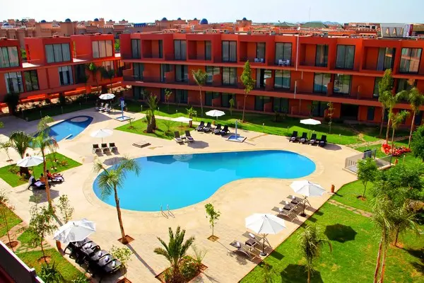 Piscine hotel Rawabi : voyage tout compris Maroc.
Vue aérienne de la piscine. entouré par l'Hôtel de briques rouge et palmiers au soleil. 
