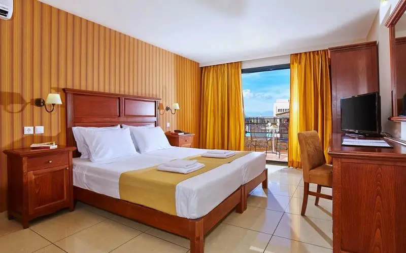 Chambre d’hôtel  Sentido Vasia Resort & Spa 5 étoiles avec lit double King size . Chambre avec meubles en bois, terrasse et superbe vue sur la mer.