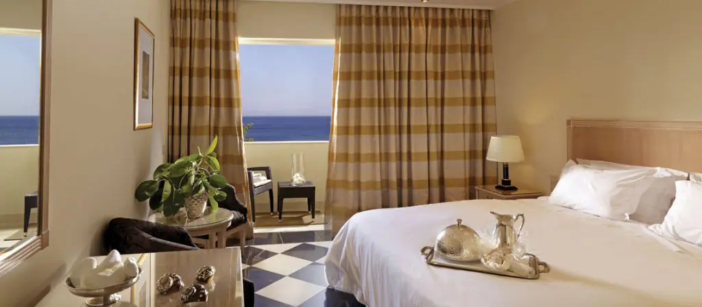Chambre de l'hôtel pour un voyage tout compris en Crète. Chambre spacieuse de l’hôtel 5 étoiles avec lit double + terrasse, plateau petit déjeuner posé sur le lit . Vue magnifique sur la méditerranée. 